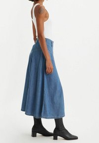 Jupe maxi en denim avec un design évasé, de couleur bleu clair, dotée d'une taille haute et d'une texture lisse. Associée à des bottines noires.