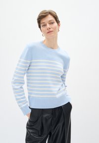 Maglione a righe blu chiaro con strisce orizzontali crema, scollatura rotonda e orlo a costine, abbinato a pantaloni di pelle nera.
