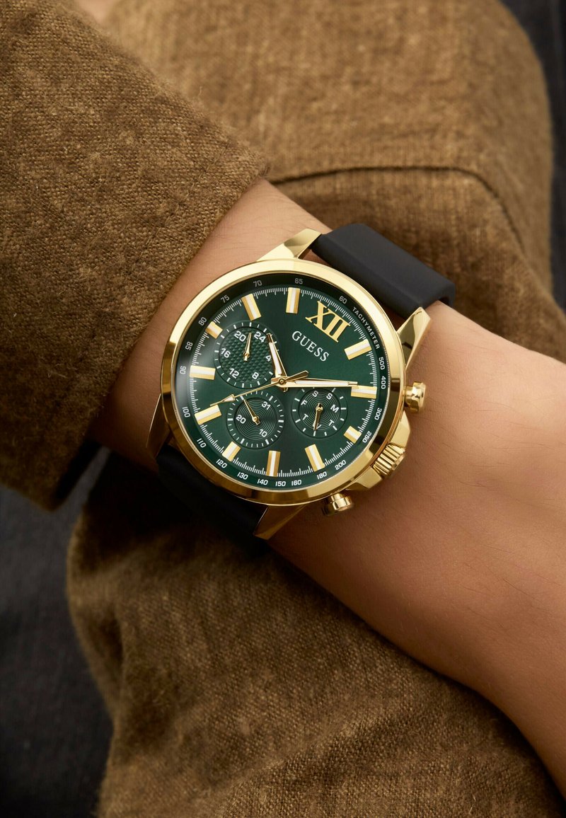 Orologio con quadrante verde e dettagli dorati, indici luminosi, tre subquadranti e cinturino in silicone nero, mostrato su un polso.