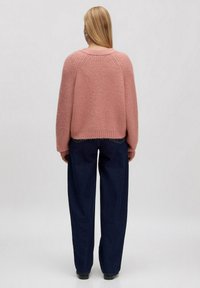 Flauschiger pinker Strickpullover mit lockerer Passform und geripptem Struktur, kombiniert mit weit geschnittenen dunkelblauen Jeans, von hinten betrachtet.