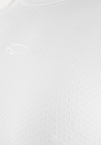Maillot de sport blanc texturé avec un petit logo flèche en relief sur la poitrine supérieure près du col.