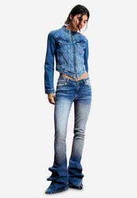 Chaqueta de mezclilla y vaqueros acampanados con un degradado de azul claro a oscuro. La chaqueta tiene una cremallera, dos bolsillos y un diseño ajustado. Los vaqueros tienen un dobladillo ancho y con volantes.