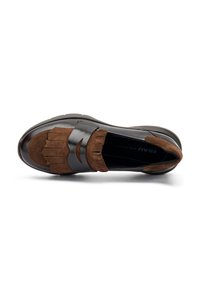 Chaussure slip-on en daim marron et cuir noir avec un design à franges et un accent courbé à l'avant, présentant une texture lisse et une forme arrondie.