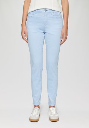 Jeans en denim bleu clair avec une coupe slim, design à cinq poches et fermeture à bouton. Portés avec des baskets blanches avec des accents tan.