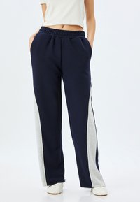 Marineblauwe sweatpants met grijze zijpanelen, elastische tailleband en twee zijzakken. Gemaakt van zacht materiaal en heeft een relaxte pasvorm.