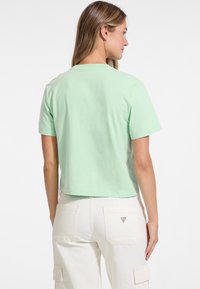 Lyhythihainen, cropped t-paita vaaleanmintunvihreästä puuvillasta, jossa on pyöreä pääntie ja sileä pinta. Valkoiset cargo-housut, joissa on takataskujen yksityiskohtia.