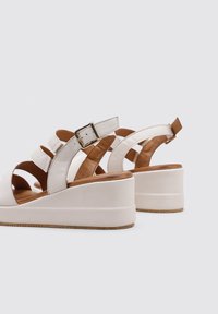 Sandalias de cuña blancas con un acabado de cuero suave, diseño de punta abierta y correa ajustable en el tobillo. Sutiles acentos marrones en la suela.