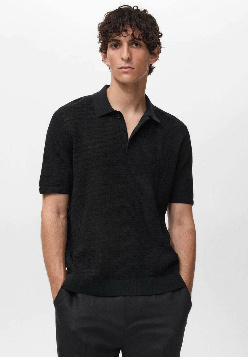 Polo shirt nero a maniche corte con design a maglia testurizzata, colletto piatto e patta con tre bottoni. Indossato con pantaloni su misura.