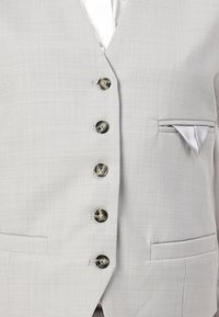 Gilet gris clair à la texture fine, doté de six boutons, d'une poche poitrine à gauche avec un mouchoir plié et de deux poches avant.