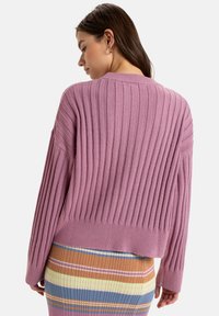 Light purple ribbed knit sweater with a cropped design and wide sleeves, paired with a colorful striped skirt. Soft texture, casual fit.