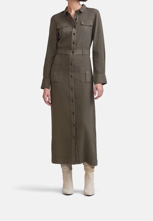 Olivengrøn langærmet midikjole med knapper foran og lommer på bryst og hofter, båret med cremefarvede løstsiddende ankelstøvler.