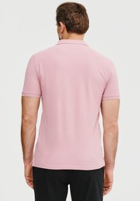 Jasnoróżowa koszula polo z krótkim rękawem, gładka w dotyku, z kołnierzykiem. Prosty wzór z prostym dołem i bez widocznych wzorów czy akcentów.