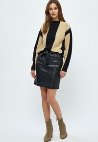 Beige en zwarte gestreepte trui met lange mouwen, gecombineerd met een zwarte leren rok met een trekkoord in de taille en een gestructureerde afwerking.