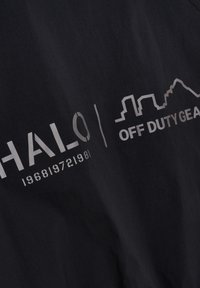 Czarna tkanina z metalicznym srebrnym napisem "HALO 1968/1972/1981" oraz "OFF DUTY GEAR." Prosty design, bez wyraźnych wzorów czy faktur.