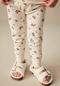 Legginsy w kremowy wzór kwiatowy z tłoczeniem, w połączeniu z bia�łymi, puszystymi sandałami z dwiema regulowanymi paskami i gumową podeszwą.