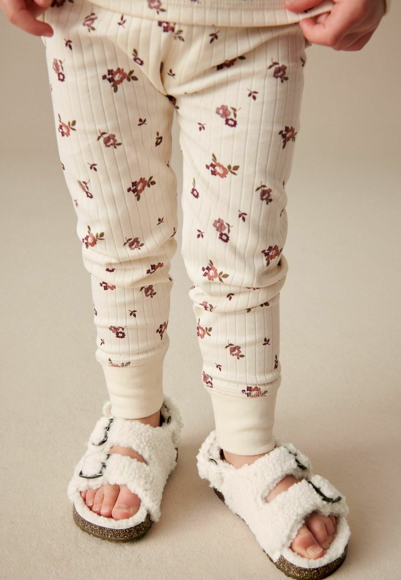 Legginsy w kremowy wzór kwiatowy z tłoczeniem, w połączeniu z białymi, puszystymi sandałami z dwiema regulowanymi paskami i gumową podeszwą.