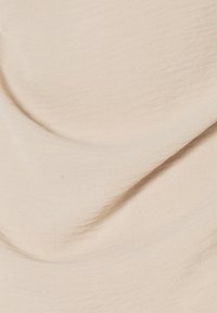 Tessuto beige con morbide pieghe naturali e una fine trama intrecciata che crea leggeri contrasti di ombre e luci.