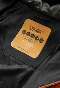 Intérieur d'une veste noire présentant une étiquette de performance ; affiche un tissu imperméable et respirant, des spécifications techniques et des instructions d'entretien.