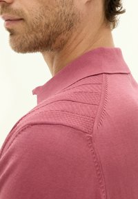 Maglietta polo a maglia rosa chiaro con colletto testurizzato e dettagli sulle spalle, corpo liscio e cuciture ordinate.