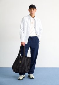 Striped button-up shirt, white t-shirt, navy sweatpants, black striped tote bag, and light-colored sneakers. Simple, casual ensemble.
