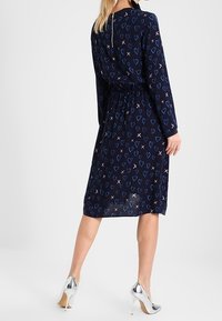 Marineblaues Kleid mit langen Ärmeln, elastischem Bund und Herz- sowie X-Mustern in Hellblau und Pink. Silberne High Heels runden den Look ab.