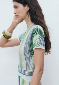 Abito in maglia con strisce verticali in verde, blu e beige. Maniche corte con bordi a coste. Texture liscia, design minimalista.