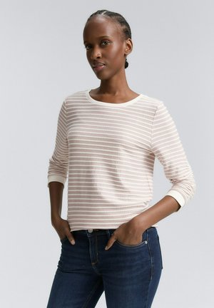 Ljust rosa randig långärmad tröja med rund halsringning och vita manschetter, kombinerad med mörkblå jeans. Mjuk textur, avslappnad passform.