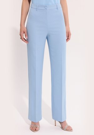 Jasnoniebieskie, dopasowane spodnie o prostych nogawkach, noszone z beżowymi sandałami na wysokim obcasie z paskami ozdobionymi kryształkami, na jednolitym tle.