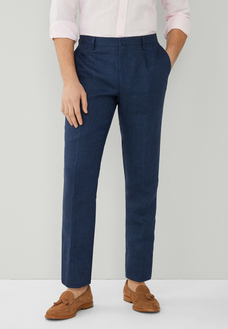 Pantaloni in lino blu navy con vestibilità slim, fronte piatto e tasche laterali, abbinati a mocassini in suede marrone.