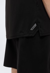 Μαύρο αθλητικό μπλουζάκι από υφή, διαπνέον ύφασμα με επίπεδη ραφή και μικρή ασημένια ετικέτα "DRYLITE" στη ραφή πλευράς.