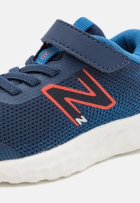 Basket bleu en maille avec un col rembourré, des lacets et une sangle Velcro. Présente un logo rouge bien visible sur le côté et une semelle en caoutchouc blanc.