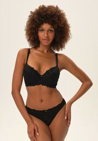 Czarny koronkowy biustonosz i pasujące stringi z regulowanymi ramiączkami; posiadają kwiatowy wzór, falbaniasty brzeg oraz mały akcent centralny.