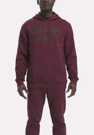 Sudadera burdeos hecha de una tela suave, con un bolsillo delantero y capucha con cordón, y un gran logo gris de Reebok en el pecho.