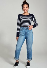 Navy blauwe en witte gestreepte bloes met lange mouwen, gecombineerd met lichtblauwe high-waisted jeans, opgerold bij de mouwen, en zwarte sneakers met witte zolen.