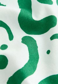Vihreät abstraktit kuviot valkoisella kankaalla, joissa on erilaisia muotoja, joissa on sileä pinta ja keskivahvuus, esittelevät leikkisää suunnittelua.