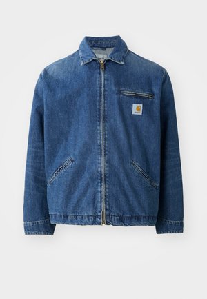 Denim jacket in medium blue with a zip front, point collar, two side pockets, and a chest pocket featuring a square logo patch.