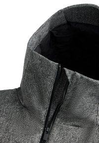 Sivý kabát s herringbone vzorom a čiernym podšitím goliera, čiastočne rozopnutý, odhaľujúci zips a ťahák.