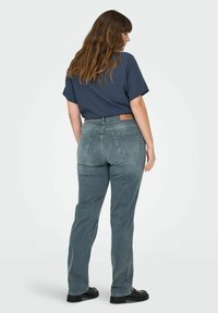 Tamno plava oversized majica i svijetlosive ravne traperice s kožnom etiketom. Traperice imaju dva stražnja džepa i izblijedjelu teksturu.