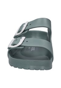 Green molded sandal with two adjustable white buckles, textured footbed, and a flat sole with raised grip pattern.
