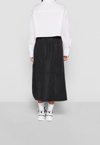 Chemise blanche courte et jupe maxi noire, présentant une texture lisse et un design simple. Portées avec des baskets blanches et des chaussettes.