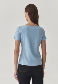 Cămașă scurtă, de culoare albastru deschis, cu gât în formă de cerc, confecționată dintr-un material neted. Croi ajustat, purtată cu pantaloni negri din denim.