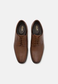 Chaussures habillées en cuir marron avec une finition lisse, bout arrondi, design à lacets et semelle intérieure rembourrée arborant la marque "Clarks Artisan".