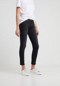 Jeans ajustados negros de denim, con una cintura de altura media, bolsillos frontales y un diseño clásico de cinco bolsillos. Combinados con zapatillas blancas.