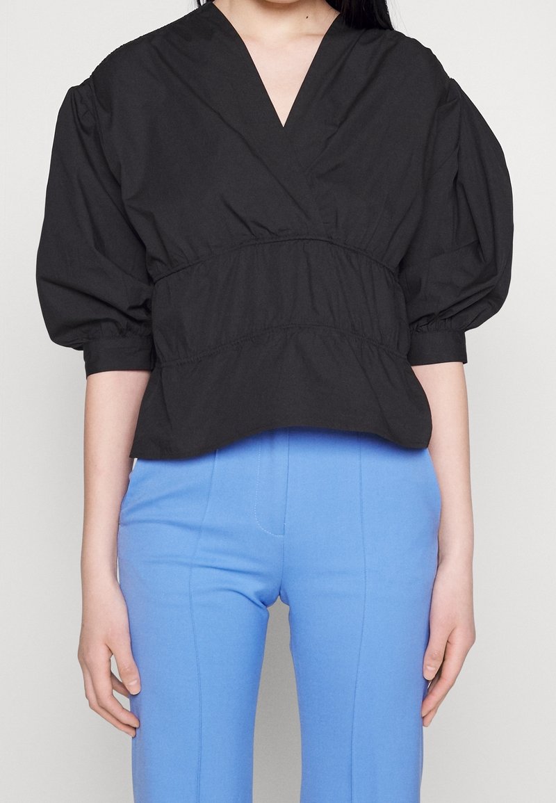 Haut court noir avec encolure en V, manches bouffantes, taille resserrée et finition texturée, associé à un pantalon ajusté bleu clair.