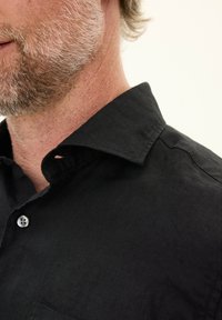 Zwarte linnen shirt met een klassieke kraag, zichtbare knoop en een gestructureerd oppervlak. Close-up van de kraag en de details van de stof.