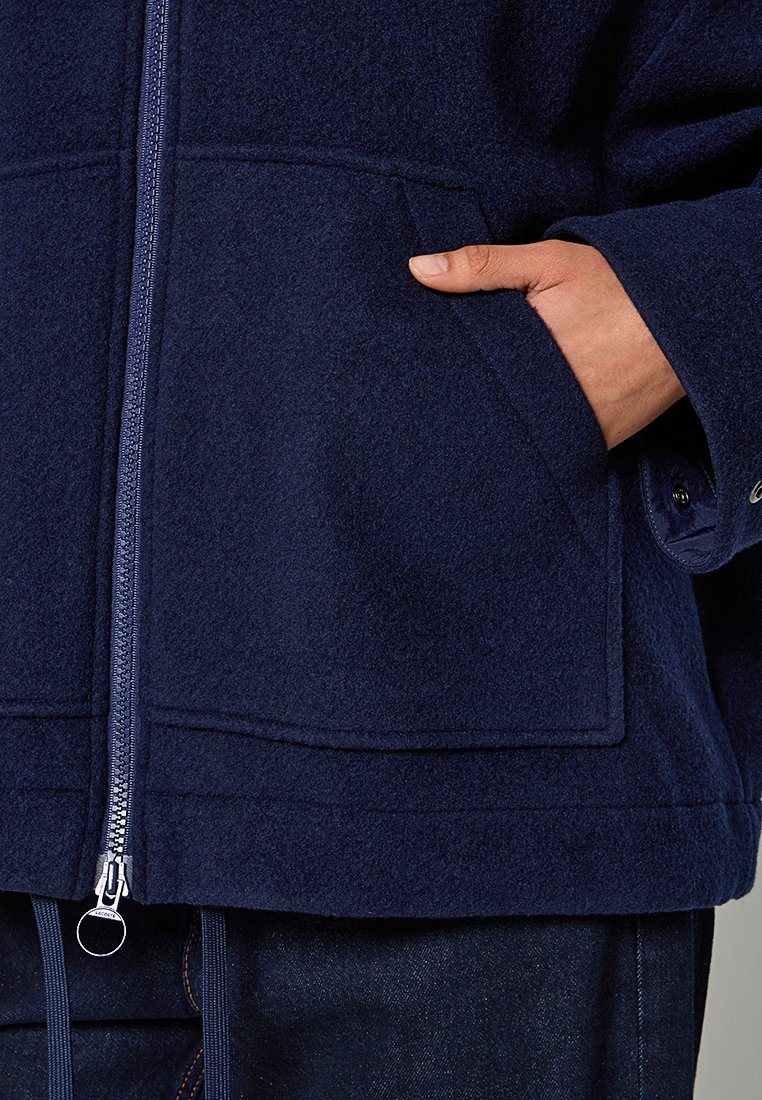 Marineblaue Fleecejacke mit Frontreißverschluss, ausgestattet mit einer aufgenähten Tasche und strukturiertem Design. Weicher Stoff, gerader Schnitt und minimales Metallzubehör.