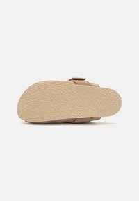 Beige sandaler med en teksturert, lys brun såle. Overdelen har et mykt materiale med et enkelt design og justerbare stroppar.
