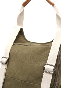 Green canvas backpack with cream straps, featuring silver hardware, a zippered pocket, and a smooth texture. Leather accent on handle.