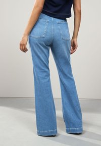 Jeans évasés bleu clair à taille haute, avec deux poches arrière et une texture en denim lisse. L'ourlet est légèrement effiloché.