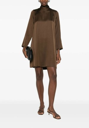 Donna che indossa un mini abito marrone a maniche lunghe con collo alto, tiene una borsa clutch nera e indossa sandali marroni con tacco basso e cinturini.